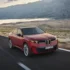 Roter BMW iX4 Elektro-Crossover der Neuen Klasse in Fahrt auf einer Asphaltstraße am Wasser
